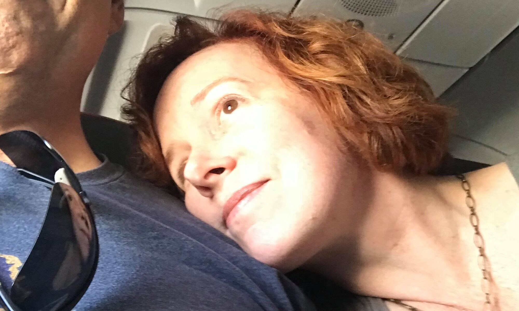 Edie White rests her right cheek against Jeremy White's chest as she peers out of an unseen airplane window.