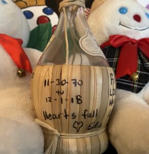 Mr. Bingle dolls flank an empty fiasco bottle. An inscription on the lower basket portion reads, "11-30-70 to 12-1-18, Hearts full, (heart) Edie."