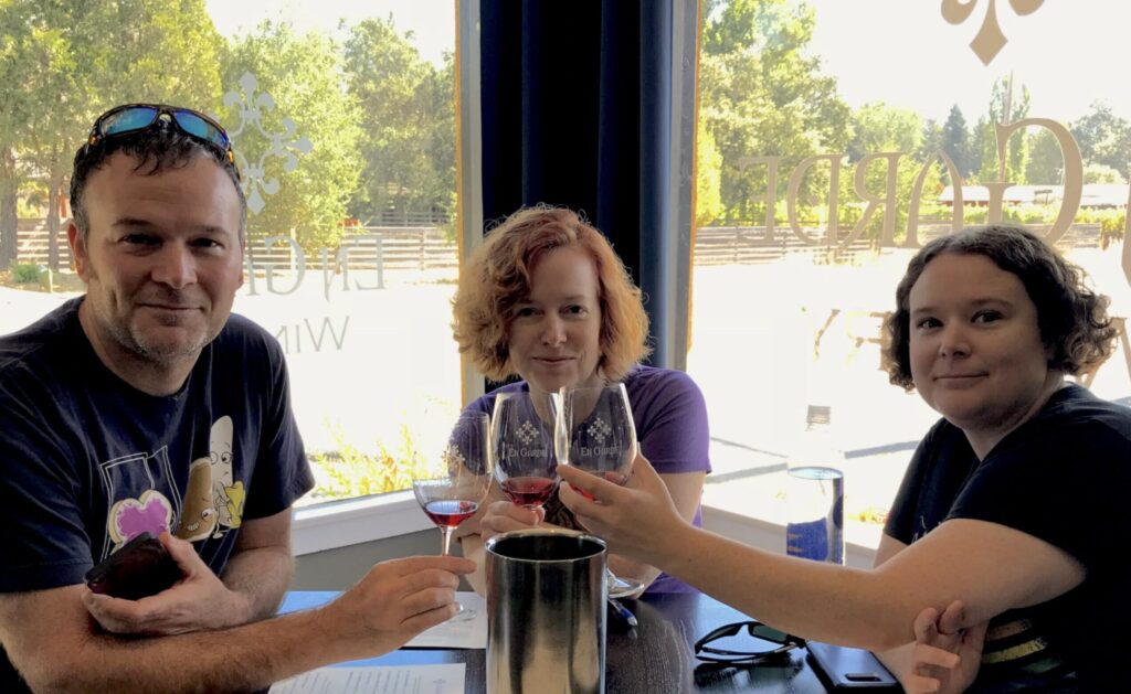 Edie White flanked by two people at a winery tasting room, each raising a glass.