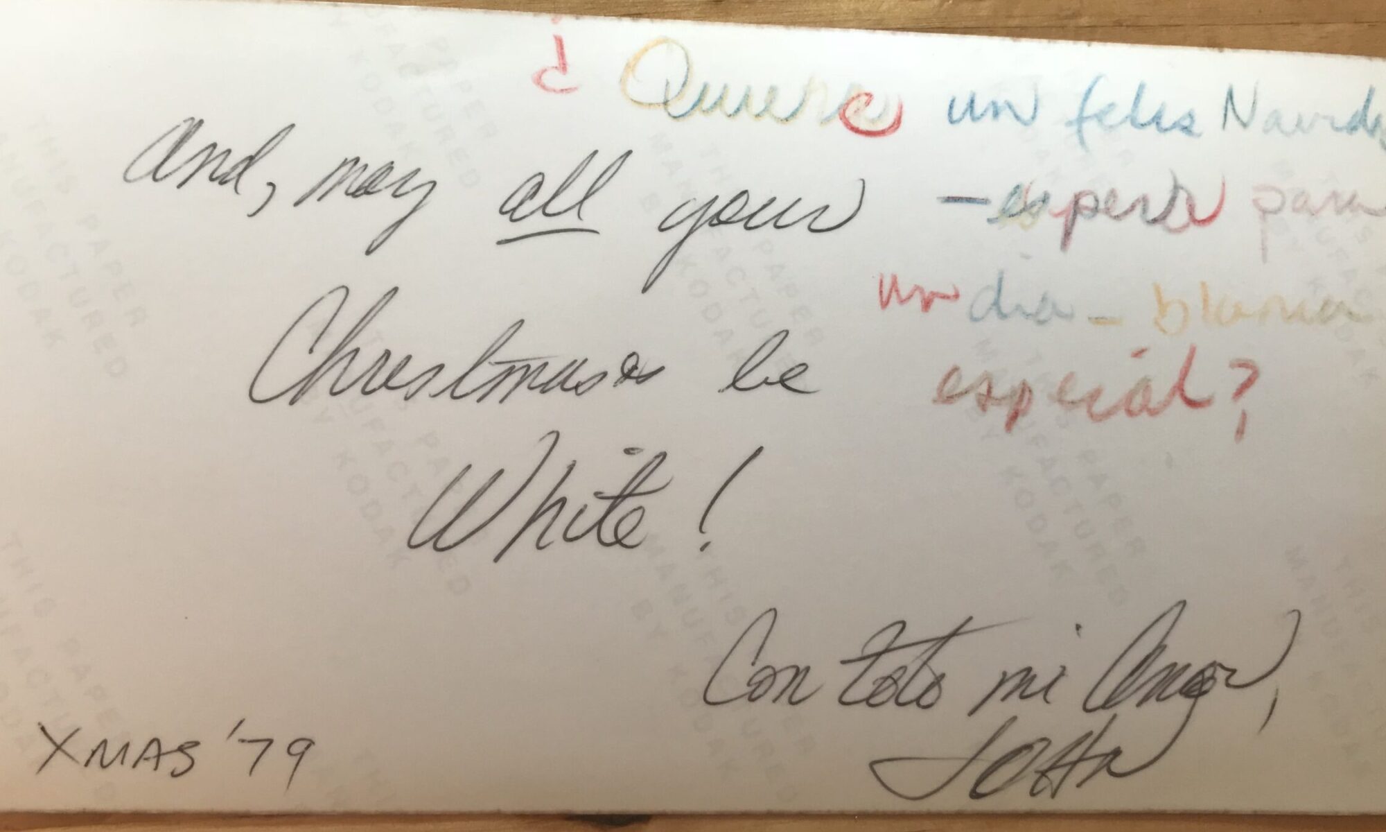 The back of a postcard from "XMAS '79" reads, "And, may *all* your Christmases be White!" in black ink, next to its Spanish translation written in four different colors. It's signed, "Con tito mi Amor, JOHN."